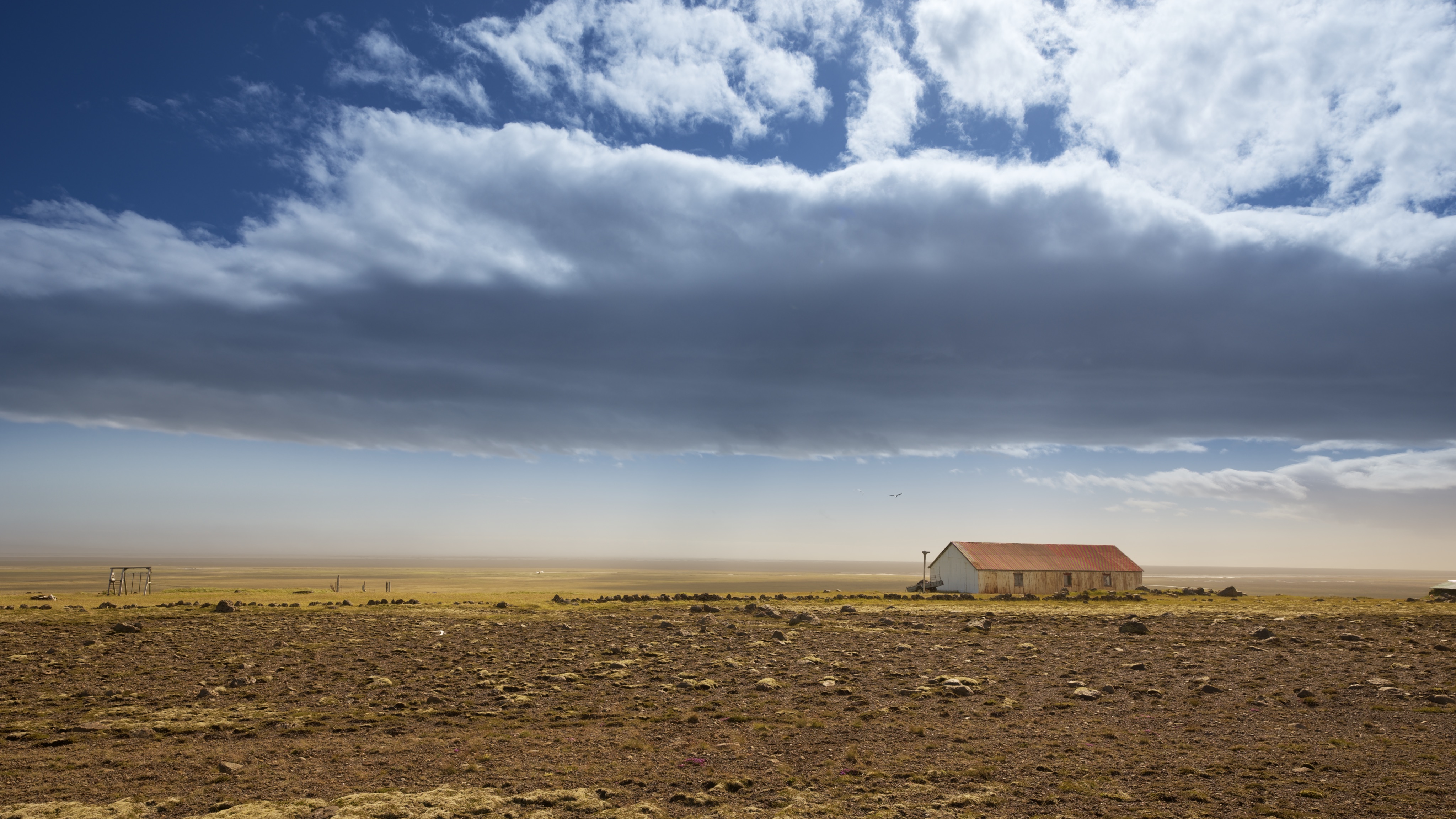 A lone house with a red roof, windswept plains under a blue cloudy sky