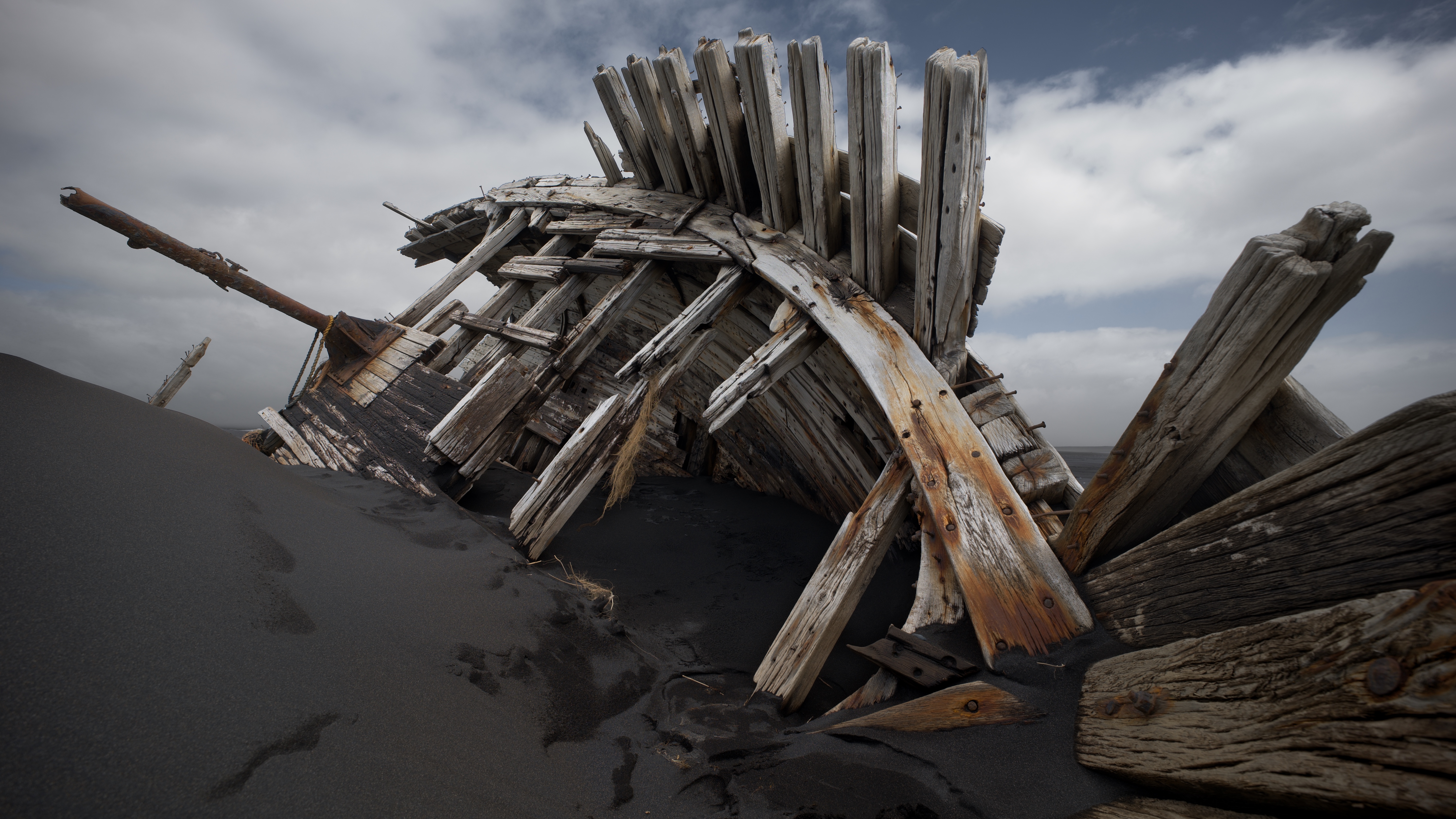 An abandoned wooden boat half buried in black sand